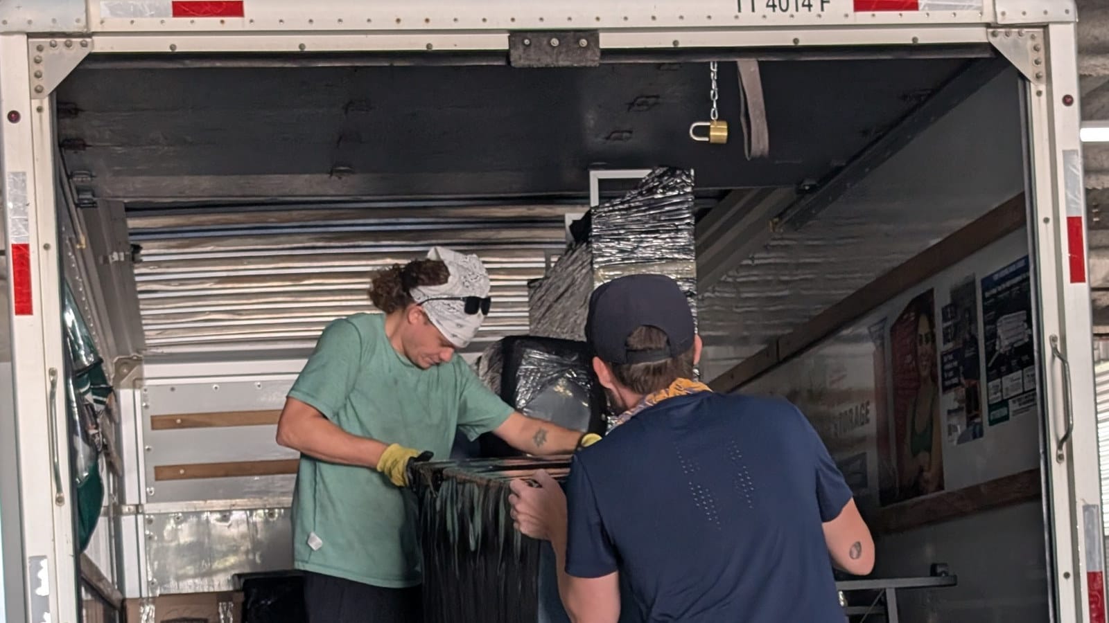 Two movers handling a protected furniture item inside the back of a moving truck.