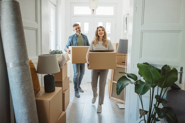 A couple carrying moving boxes into their bright new home